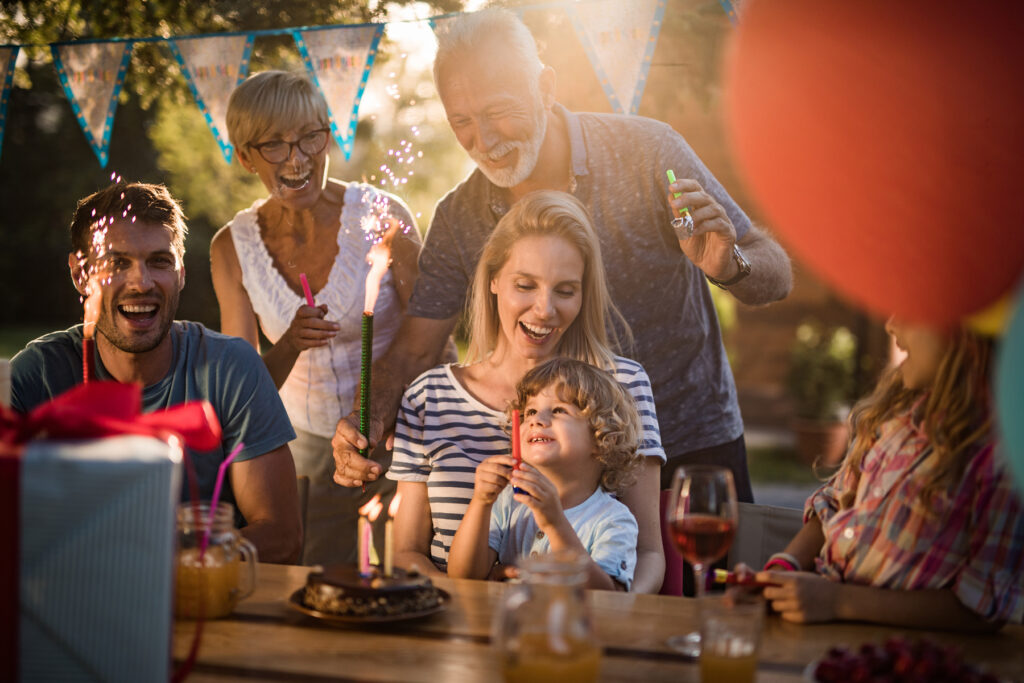Multi-generational family laughing together at an outdoor birthday celebration with sparklers