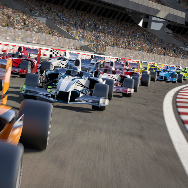 Multiple indy race cars speed through a turn on a crowded racing circuit with grandstands full of spectators in the background