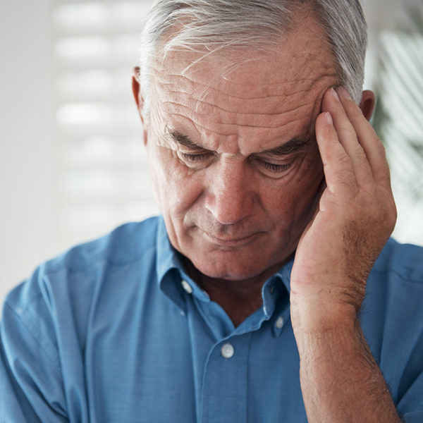 Older man holding his temple and looking distressed, representing persistent tinnitus symptoms such as ringing or buzzing in the ears.