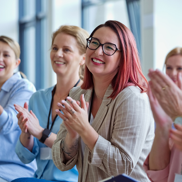 Group of women smiling and applauding at a conference or business presentation, illustrating accessible audio in professional and event settings.
