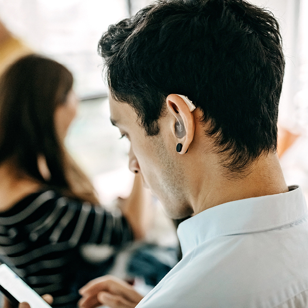 Young man wearing a behind-the-ear hearing aid in a social setting