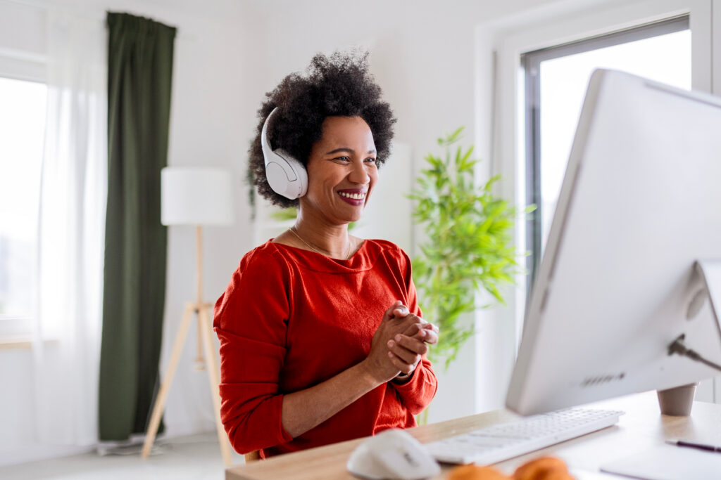 Smiling woman wearing wireless headphones at her desktop computer, completing an online hearing test