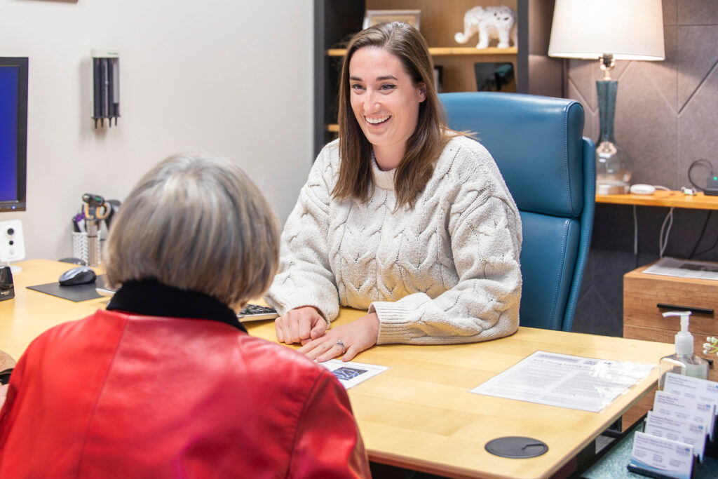 Audiologist Dr. Brittany Howard smiling and speaking with a patient across a desk in a hearing care consultation room at Family Hearing in Colorado.