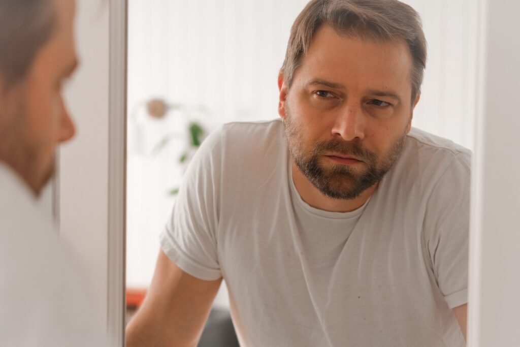 Man looking thoughtfully at his reflection in the mirror, representing the internal struggle with hearing aid stigma.