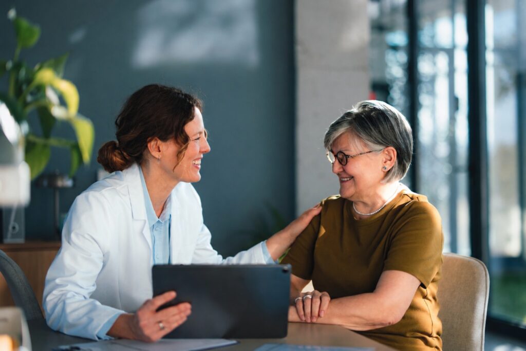 Audiologist in a white coat reviewing a tablet with a smiling senior patient during a consultation