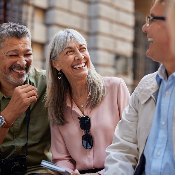 Three older adults laugh together while talking outdoors, enjoying each other's company.