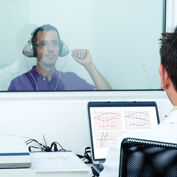 A man is receiving a hearing test inside a hearing booth